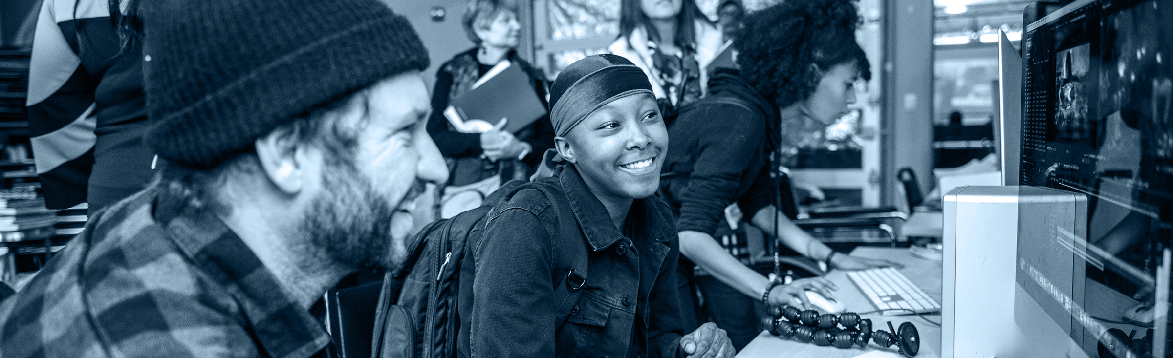 A student and teacher smiling as they look at schoolwork on a computer